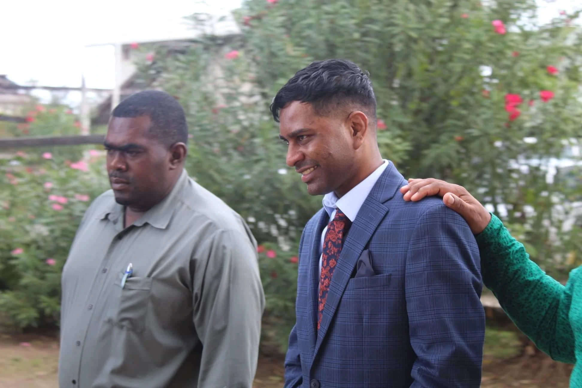 Marcus Brian Bisram in a blue suit outdoors, smiling beside another man