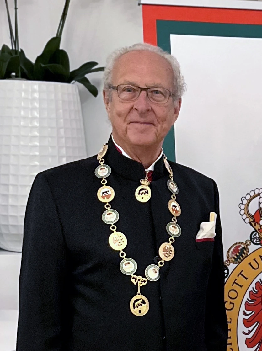 Portrait photo of an elderly man in formal black attire wearing a ceremonial chain of medallions